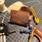 The Buccaneer on the bench with cream stitching, beside a scallop shell and tools
